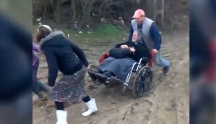 Imagini revoltătoare. O bătrână în scaun cu rotile, transportată de săteni până la ambulanţă